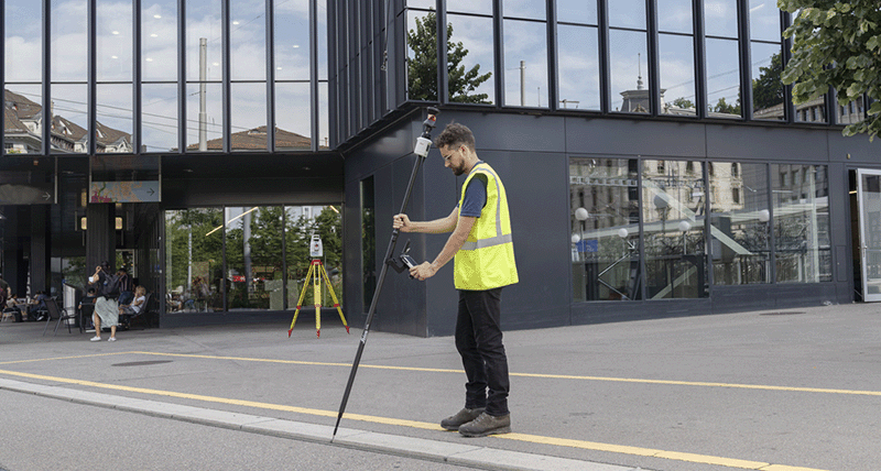 Surveyor measures a city sidewalk curb with a Leica TS16 robotic total station and a tilted AP20 prism pole.